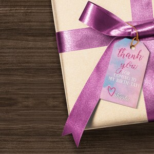 Peut inclure: Une bo&icirc;te cadeau envelopp&eacute;e de papier brun avec un ruban rose et une &eacute;tiquette qui dit "merci d'&ecirc;tre venu &agrave; mon anniversaire ! Karlie".