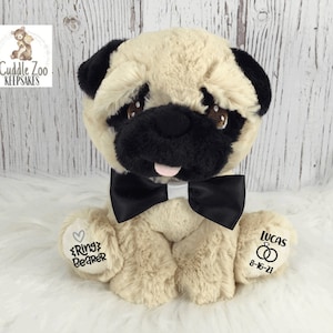 May include: A beige pug plush toy wearing a black bow tie. The plush toy has embroidered text on its paws that says "Ring Bearer" and "Lucas 8-16-21".