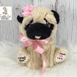 May include: A beige plush pug wearing a pink bow and a pink flower on its head. The pug has black eyes and a black nose. The pug is sitting on a white fluffy surface. The pug has a pink heart with the words "Flower Girl" embroidered on one paw and a pink rose with the name "Sarah" and the date "8-16-21" embroidered on the other paw.