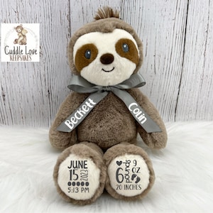 May include: A brown sloth plush toy with a gray ribbon tied around its neck. The ribbon is personalized with the names "Beckett" and "Colin". The plush toy has a white patch on its chest with the text "June 15, 2022 5:13 PM". The other foot has a white patch with the text "6 pounds 9 oz 20 inches".