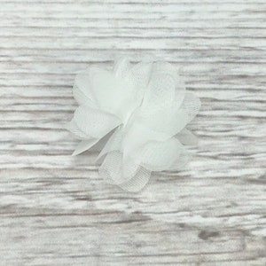 May include: A white tulle flower with a layered, ruffled design. The flower is made of soft, delicate fabric and has a simple, elegant look.