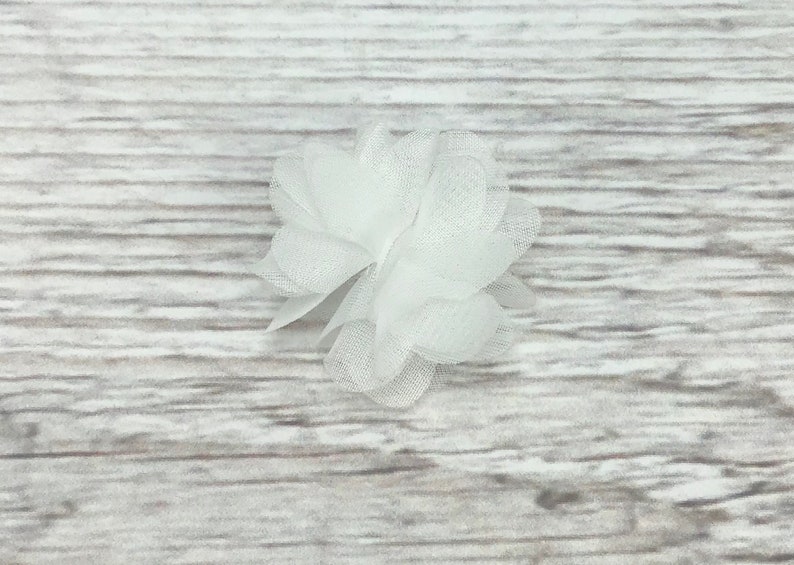 May include: A white tulle flower with a layered, ruffled design. The flower is made of soft, delicate fabric and has a simple, elegant look.