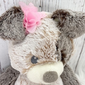 May include: A plush brown and white dog toy with a pink flower on its head.