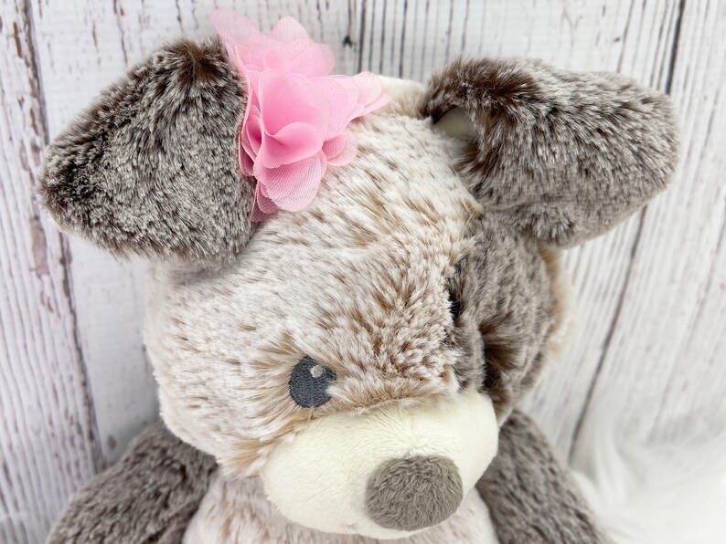 May include: A plush brown and white dog toy with a pink flower on its head.