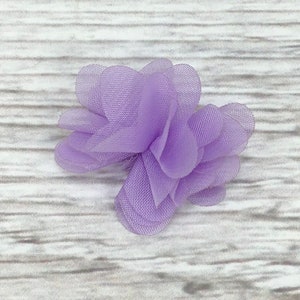 May include: A small, lavender-colored fabric flower with multiple layers of delicate, sheer fabric.