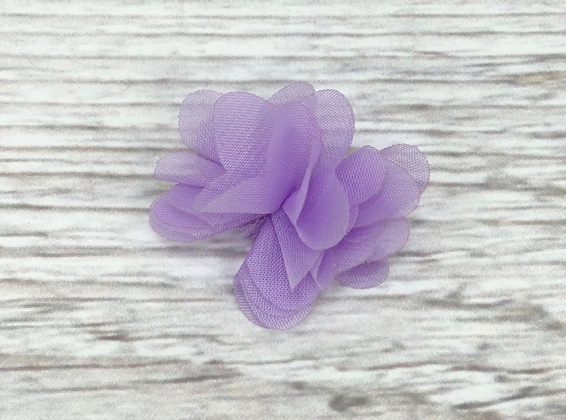 May include: A small, lavender-colored fabric flower with multiple layers of delicate, sheer fabric.