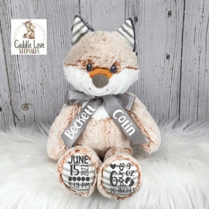 May include: A plush fox stuffed animal with a gray and white striped ear, a gray ribbon with the names Beckett and Colin, and a gray and white striped foot with the text June 15, 2022, 5:13 PM, 6 pounds 9 oz, 20 inches.