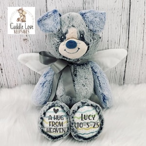 May include: A gray and blue plush angel teddy bear with wings. The bear has a heart on one foot that says "A hug from heaven" and the other foot says "Lucy 10-5-25".
