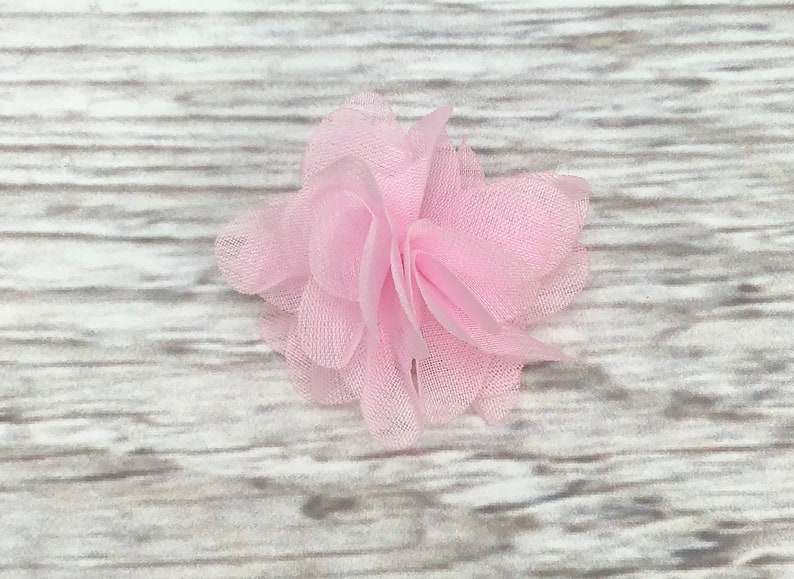 May include: A single pink fabric flower with a ruffled texture. The flower is made of soft, sheer material and has a delicate, feminine look.