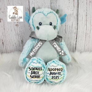 May include: A light blue plush dragon with a gray ribbon that says "My Forever Family." The dragon has embroidered details and personalized text on its feet: "Samuel Riley Smith" and "Adopted July 10, 2025."