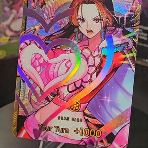 May include: A rectangular trading card featuring a holographic illustration of a character with long dark hair and purple eyes. The character forms a heart shape with hands. Text on the card reads DON!! CARD and Your Turn +1000 in bold yellow letters.