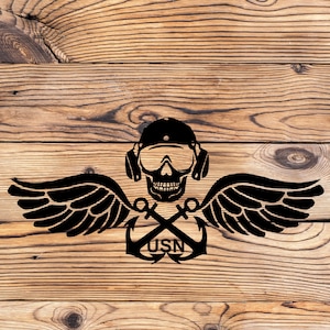 May include: Black and white illustration of a skull wearing a helmet and goggles with crossed anchors and wings. The text "USN" is below the anchors.