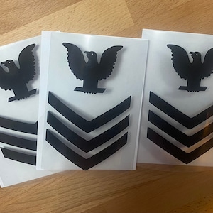 May include: Three black and white iron-on patches with a stylized eagle and three chevrons. The patches are on a white background.