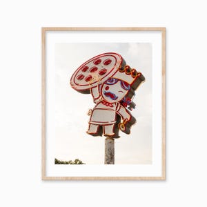 May include: A neon sign depicting a cartoon character wearing a crown and holding a pizza. The sign is red, white and blue and is mounted on a pole.