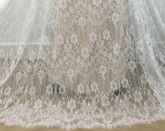 May include: White lace fabric with a floral pattern. The lace has a delicate, intricate design with small flowers and a repeating pattern.