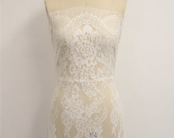 May include: White floral lace fabric draped over a mannequin. The lace features intricate floral patterns and a delicate, sheer appearance. A sparkling rhinestone necklace adorns the mannequin's neck, adding a touch of elegance to the display.