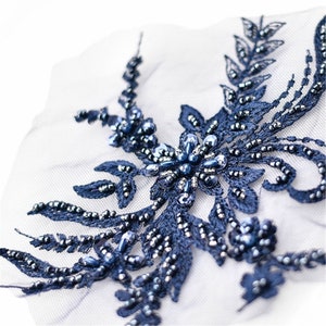 May include: Navy blue beaded floral applique with sequins. The applique is on a sheer white fabric.