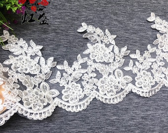 May include: White floral lace trim with a scalloped edge. The lace features detailed embroidered flowers and leaves. The trim is ideal for bridal wear, sewing projects, or adding a delicate touch to crafts.
