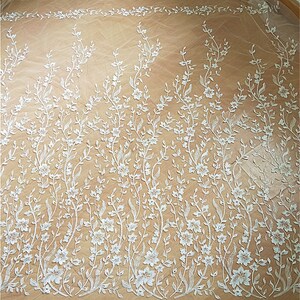 Puede incluir: Tela de encaje floral blanca con un delicado patr&oacute;n de flores y enredaderas. El encaje es transparente y tiene una textura suave y fluida.