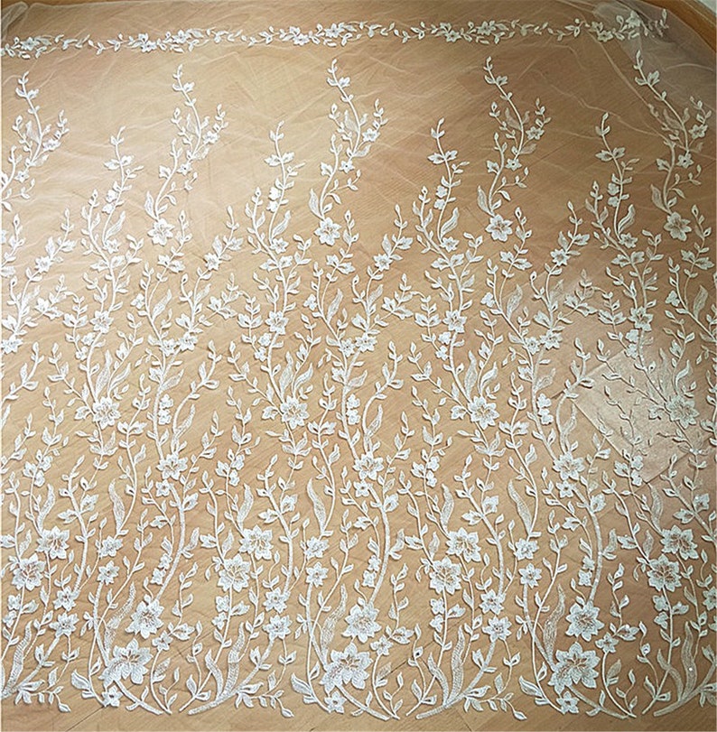 Puede incluir: Tela de encaje floral blanca con un delicado patr&oacute;n de flores y enredaderas. El encaje es transparente y tiene una textura suave y fluida.