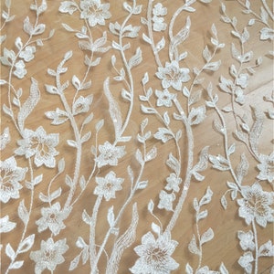 Puede incluir: Tela de encaje floral blanca con un delicado patr&oacute;n de flores y hojas. El encaje es transparente y tiene una textura suave y fluida.