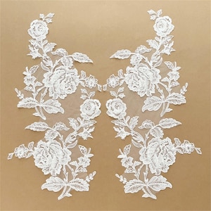 May include: Two white lace appliques with floral designs. Each applique features a large flower with smaller flowers and leaves surrounding it.
