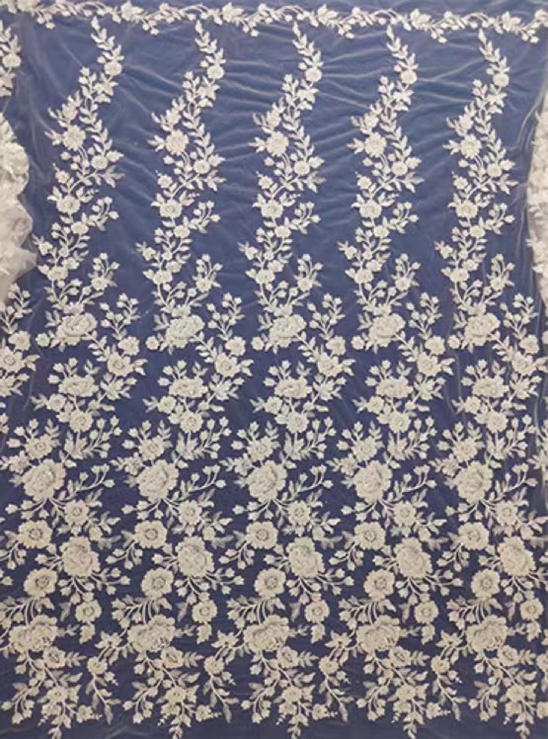 May include: White floral embroidered lace fabric with a delicate pattern. The lace is on a sheer mesh background.