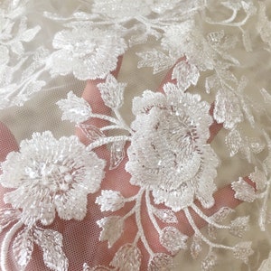 May include: White floral lace fabric with a delicate pattern of flowers and leaves. The lace is beaded and has a subtle shimmer.