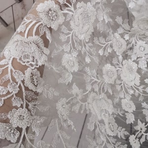 May include: White beaded floral lace fabric with a delicate pattern. The lace is sheer and has a soft, flowing texture.