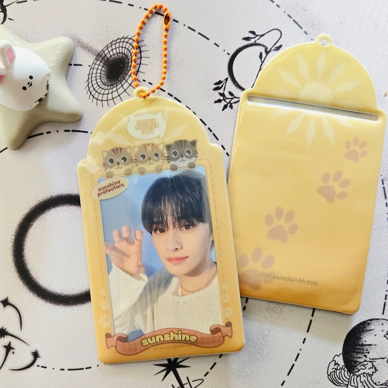 May include: A yellow plastic card holder with a photo of a young man with black hair. The card holder has a picture of three cartoon cats and the text "sunshine protectors" and "sunshine". The back of the card holder is yellow with a sun and paw prints.