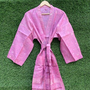 May include: A pink cotton robe with a floral print and a tie belt. The robe has long sleeves and a V-neck.