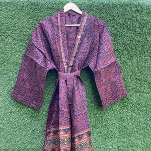 May include: A long, red and black patterned kimono with a gold trim. The kimono has a tie belt and long sleeves.