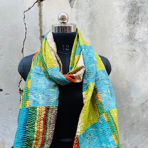 May include: A colorful patchwork silk scarf with a variety of colors and patterns, including green, blue, orange, and red. The scarf is draped over a black mannequin.