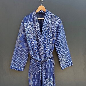 Könnte beinhalten: Eine blaue und weiße gesteppte Robe mit einem Bindegürtel. Die Robe hat ein Patchwork-Design mit verschiedenen geometrischen und floralen Mustern.