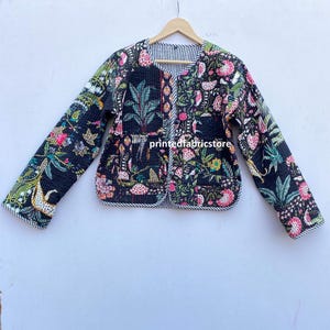 Puede incluir: Una chaqueta acolchada negra con estampado floral y ribete blanco y negro a rayas. La chaqueta tiene cierre de botón y mangas largas.