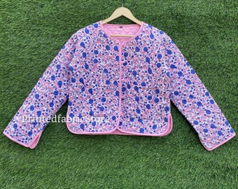 May include: A quilted jacket with a floral pattern in blue and white on a pink background. The jacket has a round neckline and long sleeves. The edges are trimmed with pink piping. The text "Printedfabricstore" is visible on the left sleeve.