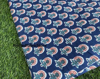 May include: A close-up of a blue fabric with a repeating pattern of pink and green flowers. The fabric is folded and the edge is visible.