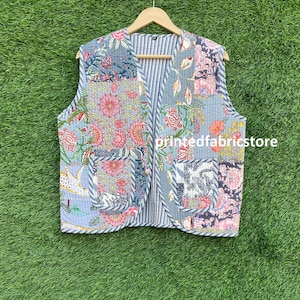 May include: A blue and white quilted vest with a floral print. The vest has a V-neck and a striped lining. The vest is made of cotton and is perfect for layering.