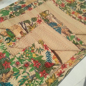 Puede incluir: Una colcha kantha beige con estampado floral y de p&aacute;jaros. La colcha est&aacute; doblada en tres partes, mostrando el intrincado detalle de la costura a mano.