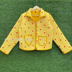 May include: Yellow quilted jacket with vertical white stripes and red heart accents. Features two heart-shaped pockets and a heart design on the front. The jacket has a collared neckline and wooden buttons. The text "PrintedfabricStore" is visible.