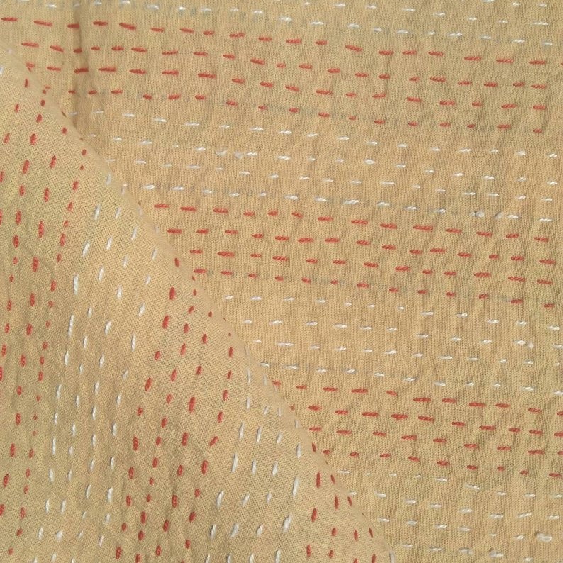 Puede incluir: Tela beige con un patr&oacute;n de cuadr&iacute;cula de puntadas rojas y blancas.