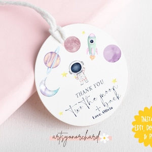 May include: Round white thank you tag with a watercolor illustration of planets, stars, a rocket, and an astronaut. The text reads "Thank you two the moon + back Love, Olivia" and "artsyonorchard".