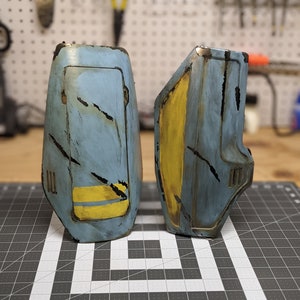 May include: Two blue and yellow painted metal pieces with a distressed look. The pieces have a rectangular shape with a yellow stripe and a small rectangular opening.