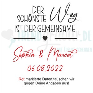 May include: A white card with black text that reads "Der sch&ouml;nste Weg ist der gemeinsame" with a black heart and a line underneath. Below the text is "Sophia & Marcel" in red cursive writing and the date "06.08.2022" in red. The text "Rot markierte Daten tauschen wir gegen Deine Angaben aus!" is in red at the bottom of the card.