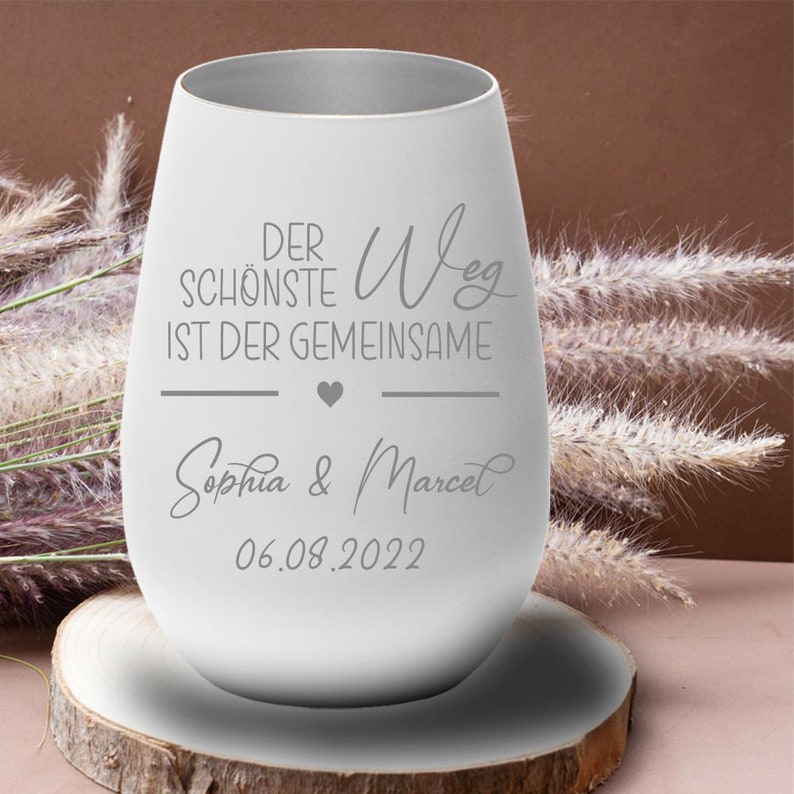 May include: White stainless steel wine tumbler with the text "Der sch&ouml;nste Weg ist der gemeinsame" and a heart symbol. Below the text is "Sophia & Marcel" and the date "06.08.2022".