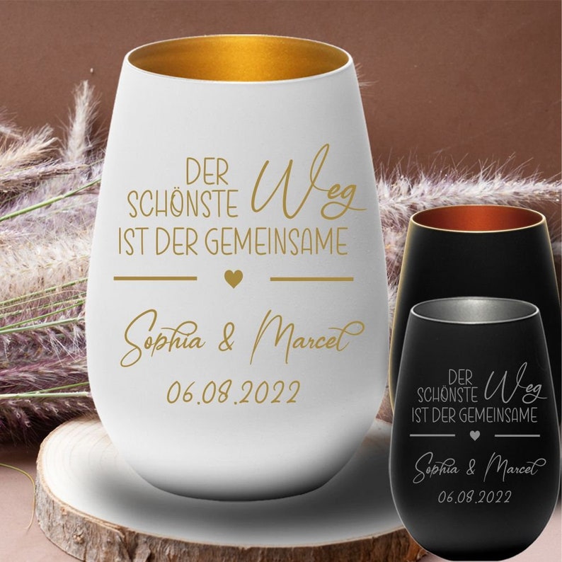 May include: Two white and black wine glasses with gold lettering. The text reads "Der sch&ouml;nste Weg ist der gemeinsame" and "Sophia & Marcel" with the date "06.08.2022".