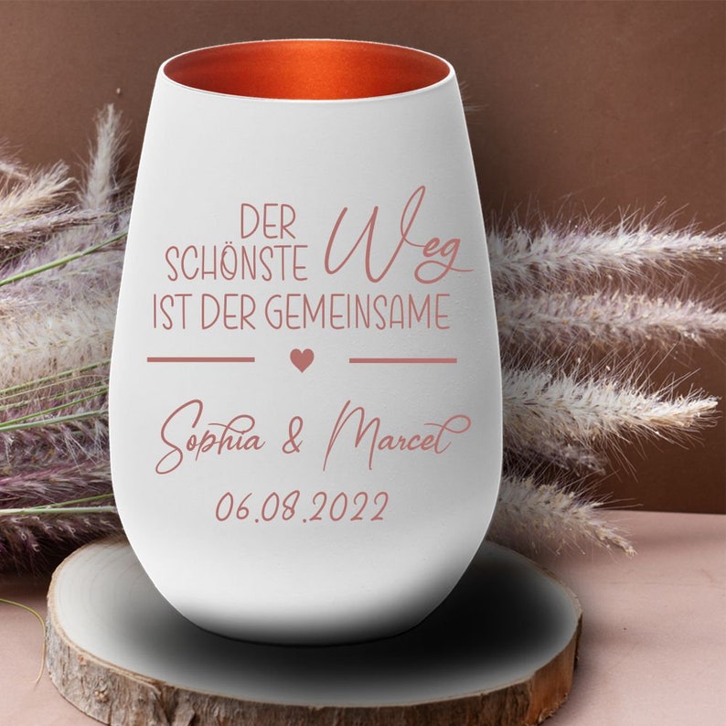 May include: White ceramic wine glass with a copper rim. The glass has the text "Der sch&ouml;nste Weg ist der gemeinsame" with a heart symbol and the names "Sophia & Marcel" and the date "06.08.2022" in a pink script font.
