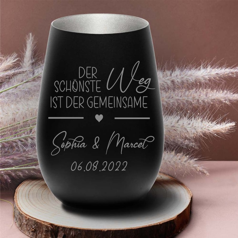 May include: Black stainless steel wine tumbler with a silver rim. It has the text "Der sch&ouml;nste Weg ist der gemeinsame" with a heart symbol and the names "Sophia & Marcel" and the date "06.08.2022" engraved on it.