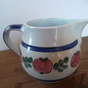 Könnte beinhalten: Eine weiße Keramikkanne mit einem blauen und grünen Apfeldesign. Die Kanne hat eine breite Öffnung und einen Henkel.