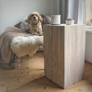 Könnte beinhalten: Ein weißer Holz-Beistelltisch mit einer grob gefertigten Textur. Der Tisch ist quadratisch und hat ein schlichtes Design. Eine weiße Tasse und eine kleine Schale stehen auf dem Tisch.